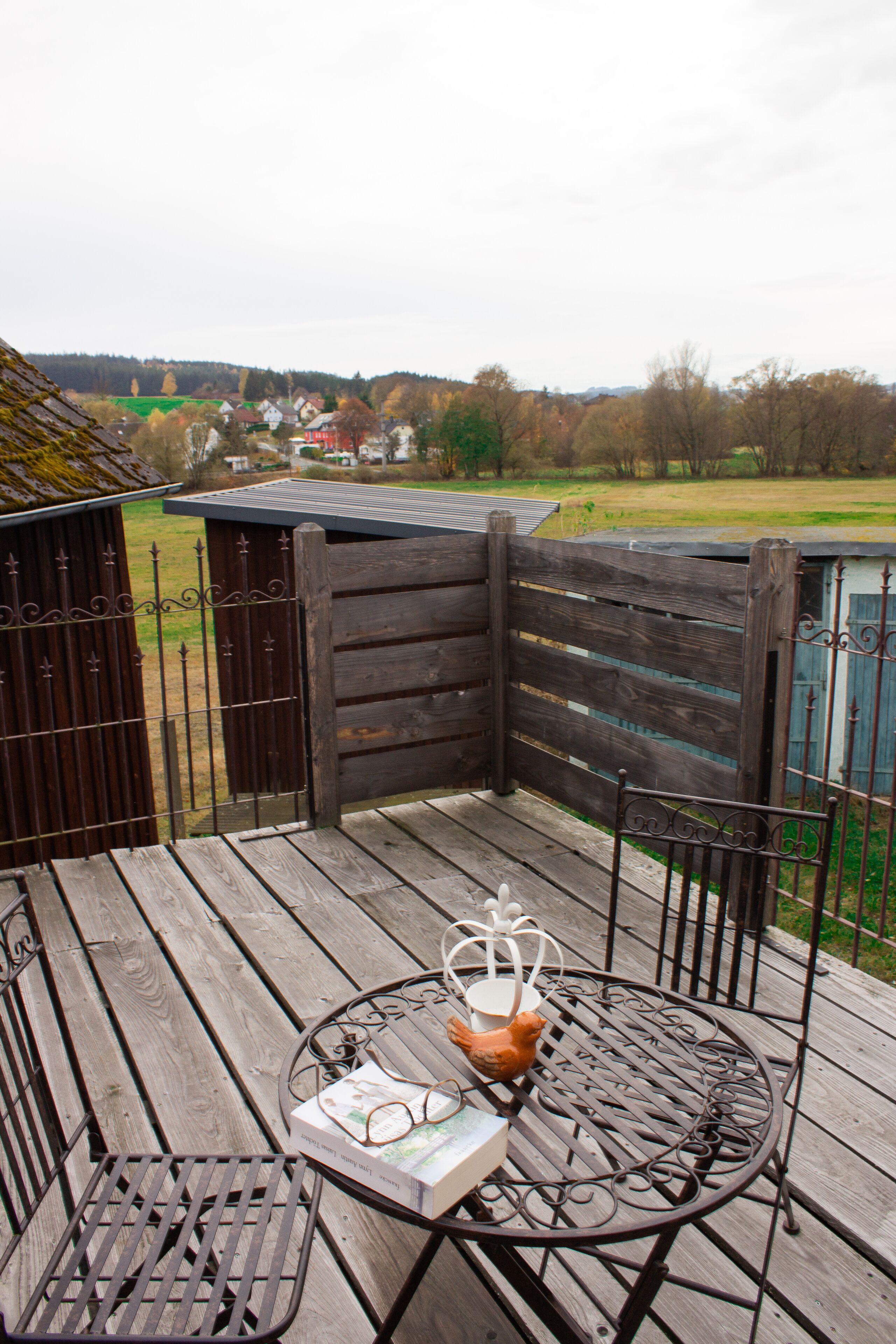 A wooden deck with a metal table and chairs, a book, and a decorative item.