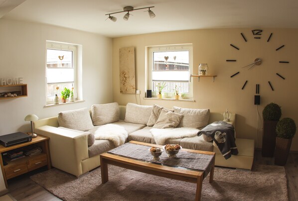 A living room with a sofa, coffee table, and a large wall clock. - Ferienhaus Deko-Scheune (Naila)