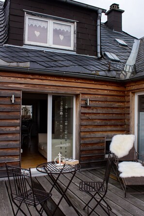 A wooden deck with a table and chairs, a sliding glass door, and a window with heart-shaped decorations. - Ferienhaus Deko-Scheune (Naila)