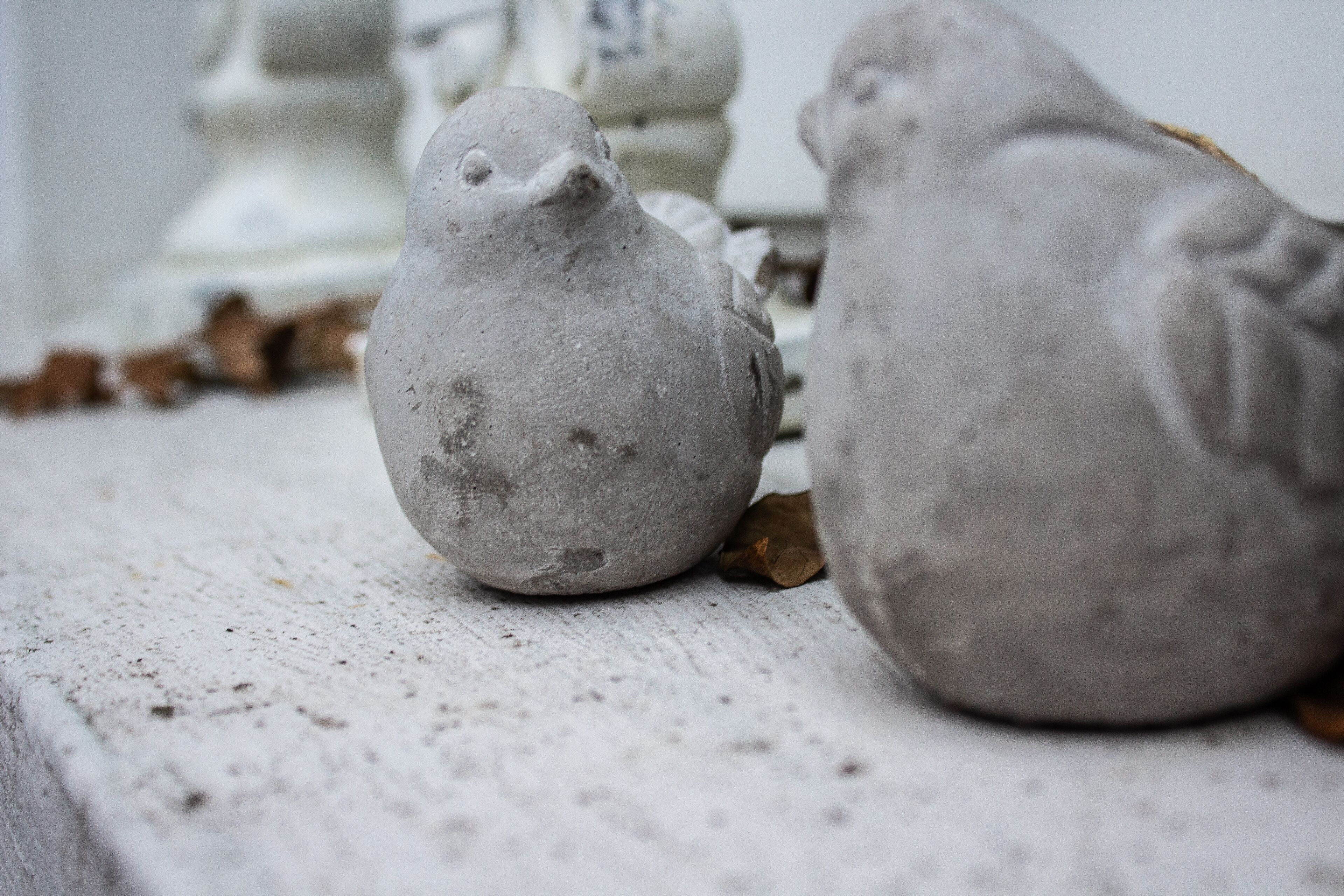 Gros plan sur deux sculptures d’oiseaux en céramique grise, posées sur une surface texturée.