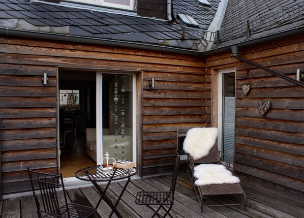 A wooden cabin with a patio area featuring a table and two chairs with white fur throws. - Ferienhaus Deko-Scheune (Naila)