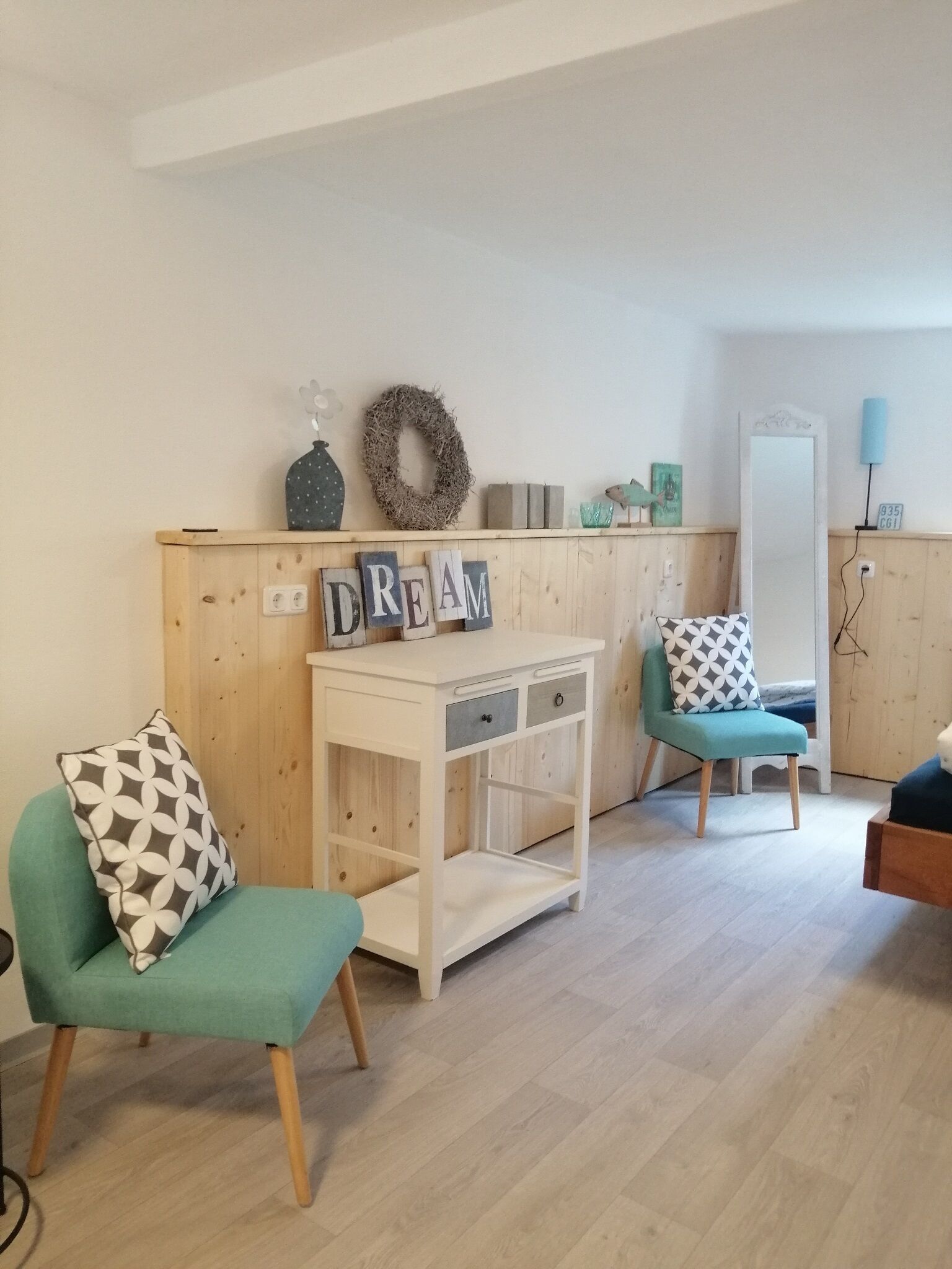 A cozy room with two teal chairs, a white table with drawers, and a wall decorated with a wreath and the word "DREAM" spelled out in letters.
