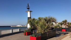 A coastal promenade with a lighthouse, palm trees, and a white fence. - Apartment T3 located in front of the beach of QUIBERON. (QUIBERON)