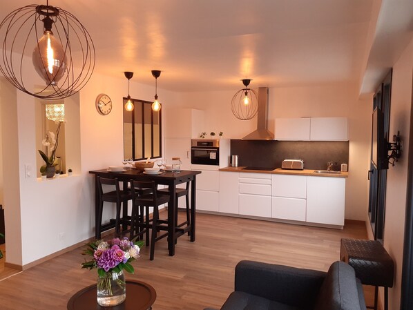 A modern kitchen with white cabinets, a dining area with a wooden table and chairs, and a living area with a sofa and a coffee table.