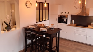 A modern kitchen with white cabinets, a wooden dining table with four chairs, a clock on the wall, and pendant lights. - Apartment T3 located in front of the beach of QUIBERON. (QUIBERON)