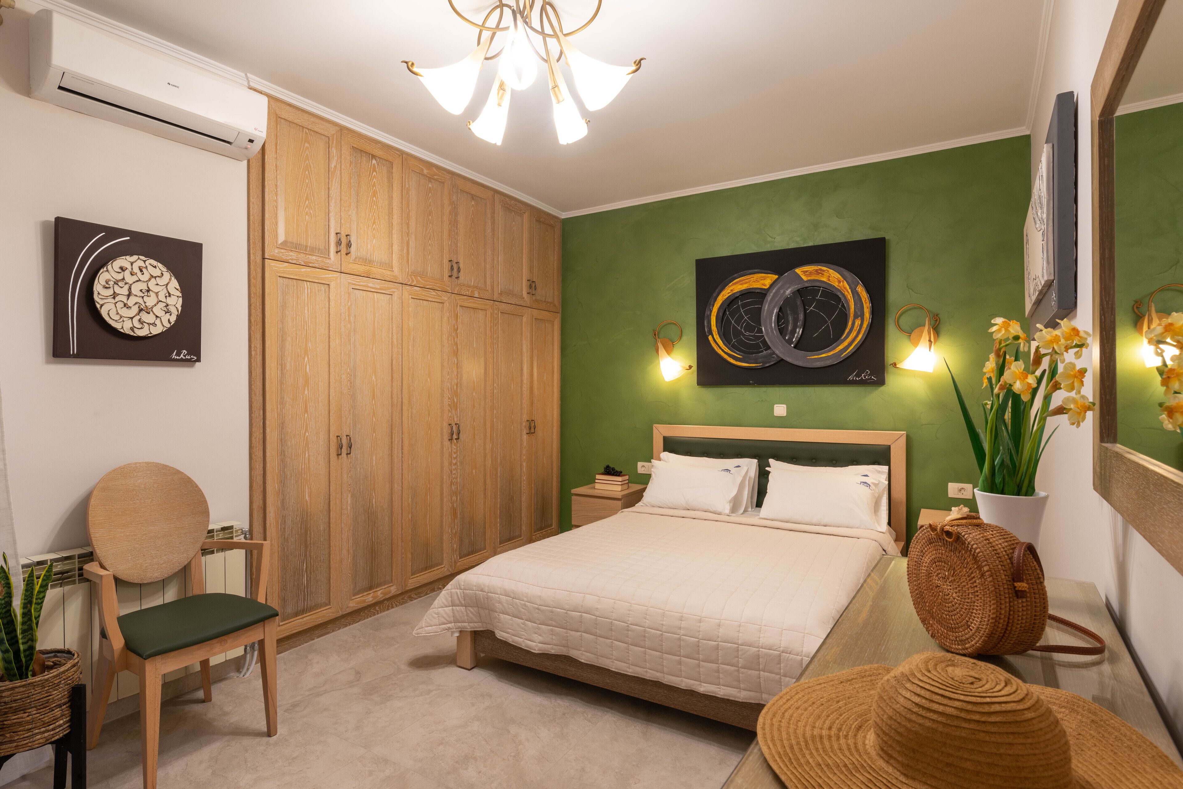 A bedroom with a bed, wooden wardrobe, wall art, and a potted plant.