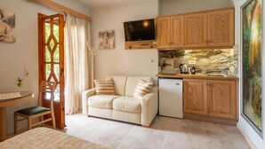 A cozy room with a sofa, a small table, a TV, wooden cabinets, and a painting. - Villa Haroula (Parga)