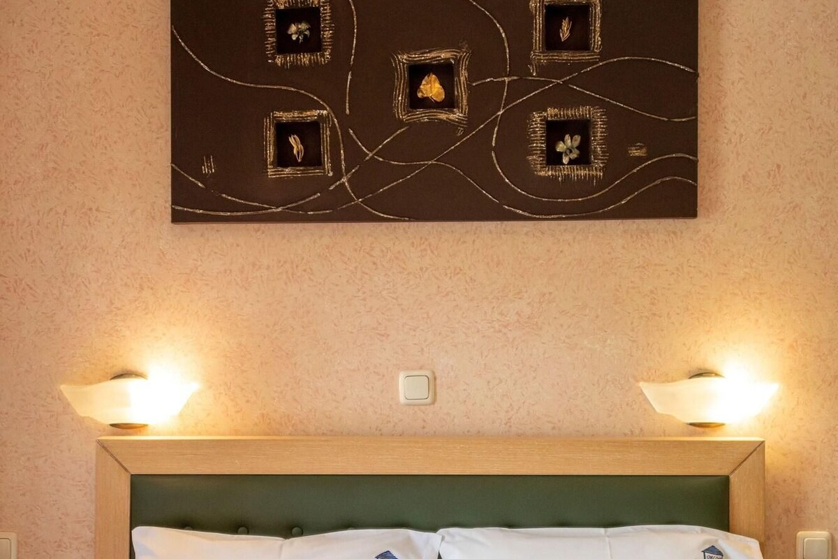A hotel room with a bed, two pillows, a headboard, and a wall-mounted artwork.