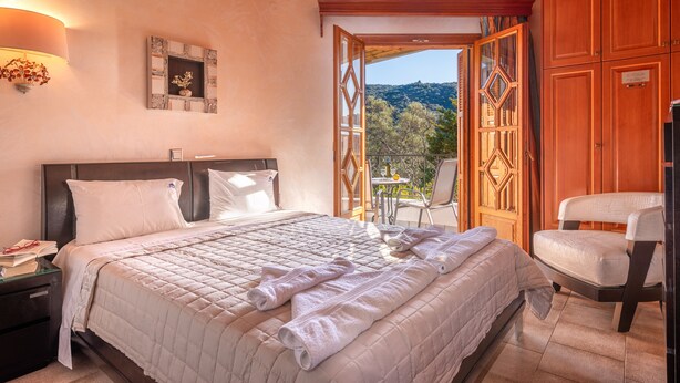 A bedroom with a large bed, a nightstand, a wooden wardrobe, and a view of the outdoors. - Villa Haroula (Parga)