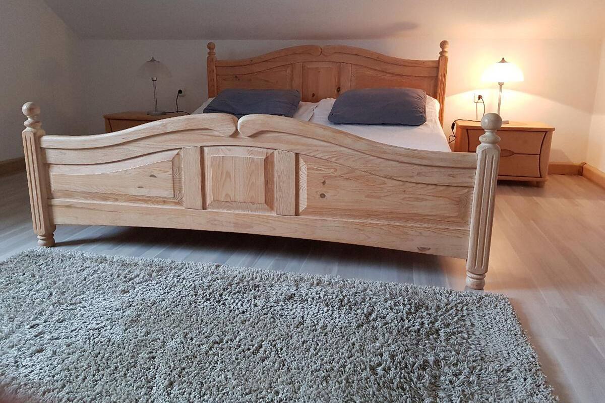 Een houten bed met hoofdeinde, twee kussens, een nachtkastje en een lamp.