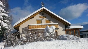 Un chalet doté d’un toit en pente, d’un balcon en bois et d’un jardin recouvert de neige.