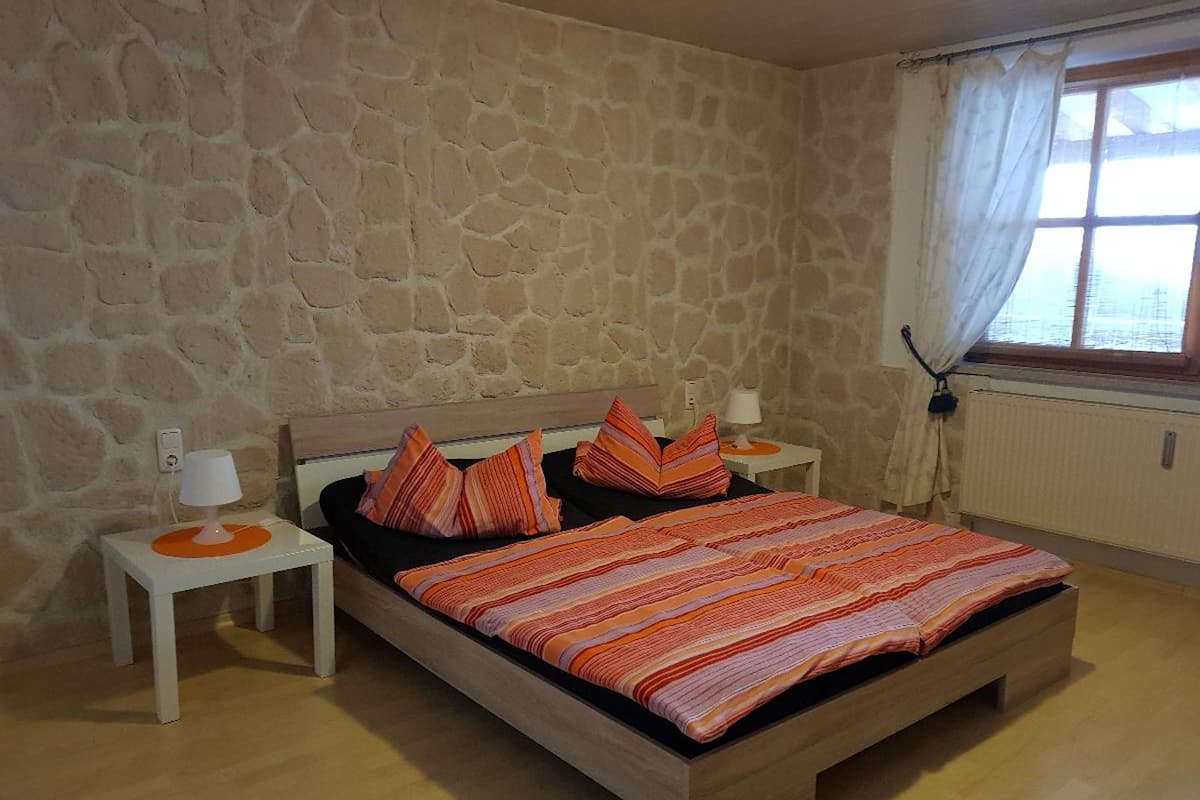 Een slaapkamer met een stenen muur, een houten bed, twee nachtkastjes met lampen en een raam met gordijnen.