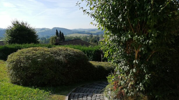 Un camí empedrat que serpenteja per un jardí ben cuidat, amb vistes a les colines llunyanes.