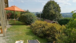 Un pati amb jardí, taula i cadires, una pèrgola de fusta i vistes al camp.