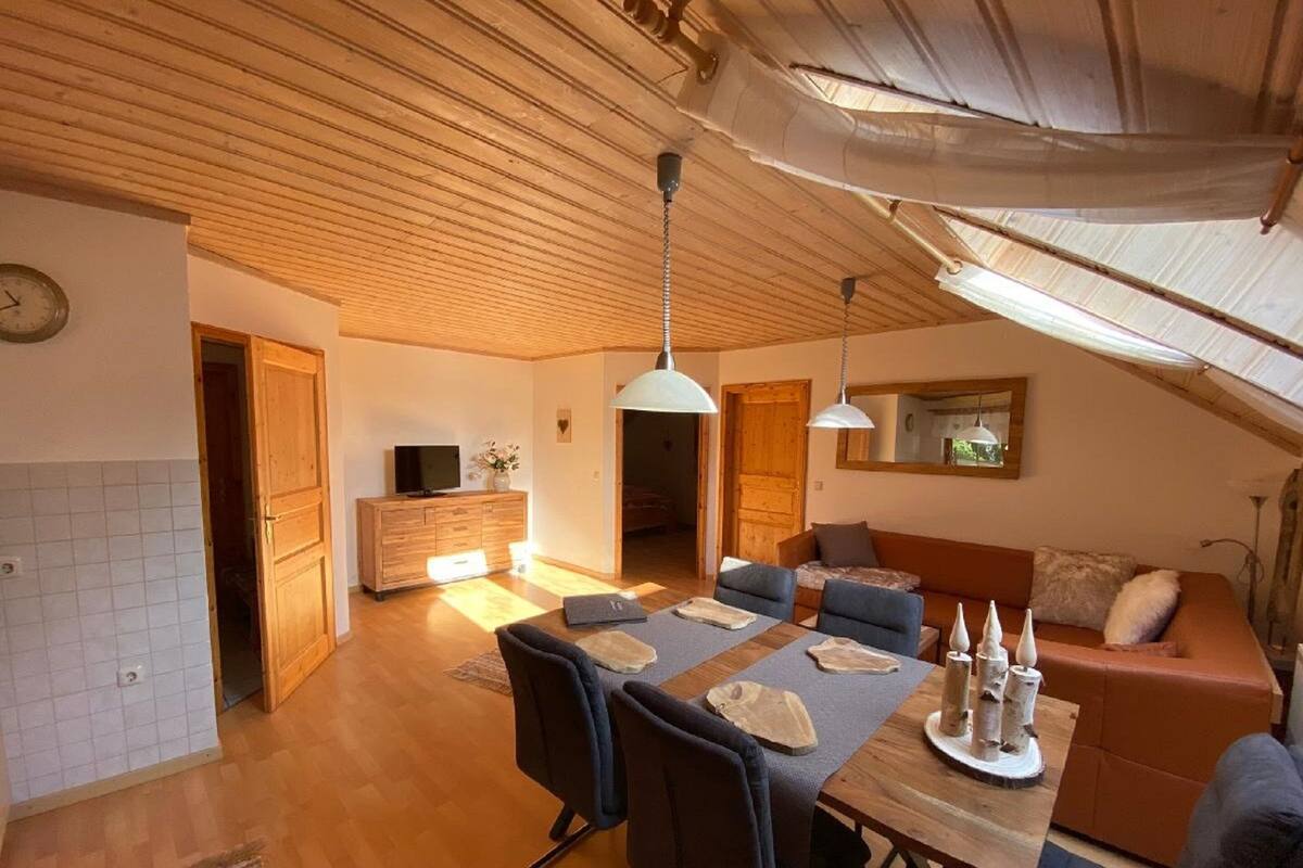 Ein geräumiger Wohnbereich mit Holzboden, einem Esstisch mit Stühlen, einer Couch und einem Fernseher auf einer Holzkommode.