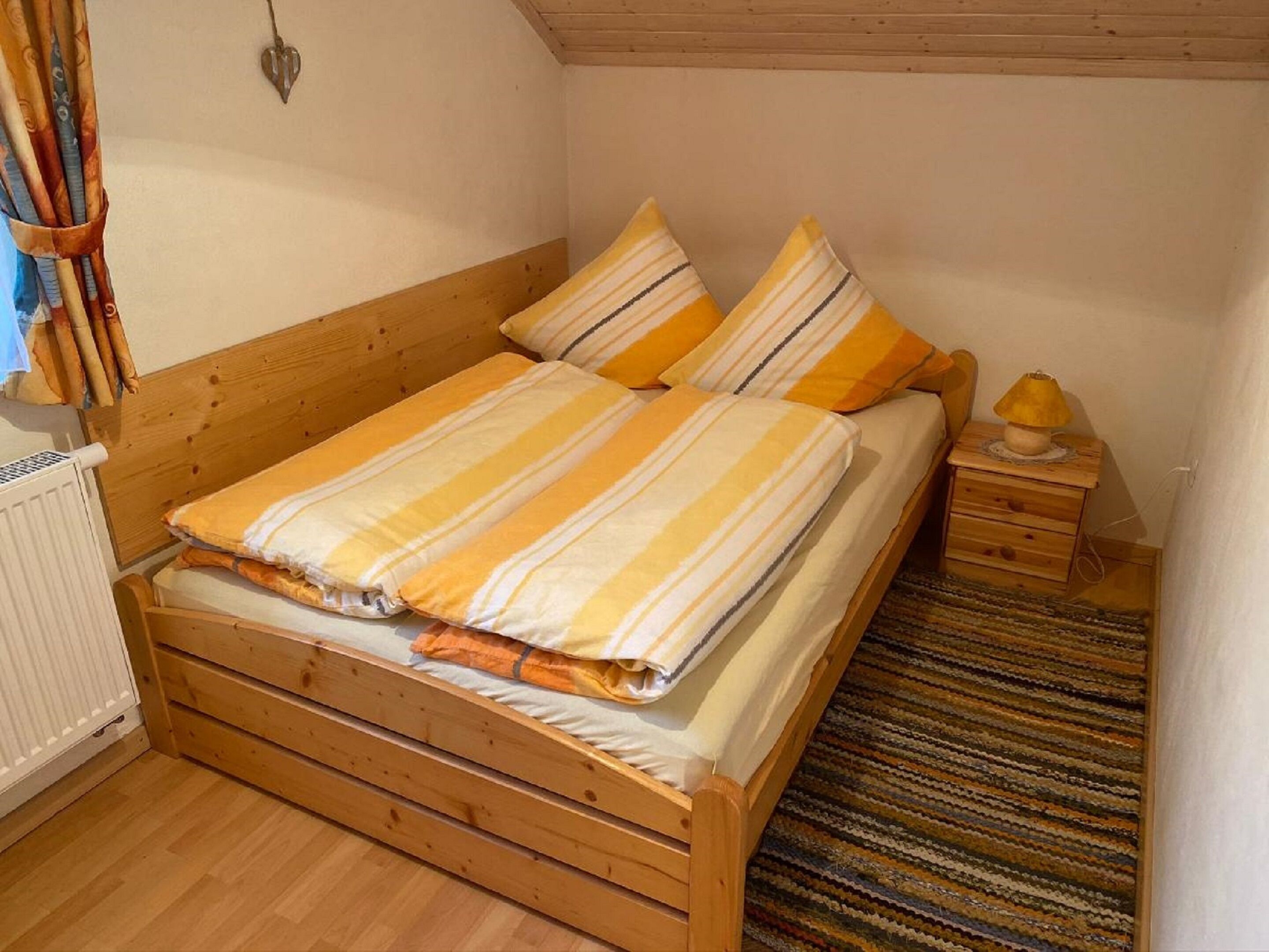 Ein hölzernes Bett mit gestreifter Bettwäsche und ein Nachttisch mit Lampe.