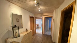 Een hal met houten vloer, een spiegel, een klein tafeltje met een vaas en een deur naar een andere kamer.