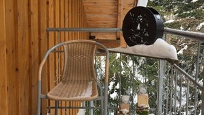Een houten blokhut met een overdekte veranda, een metalen stoel en een sneeuwbedekte reling.