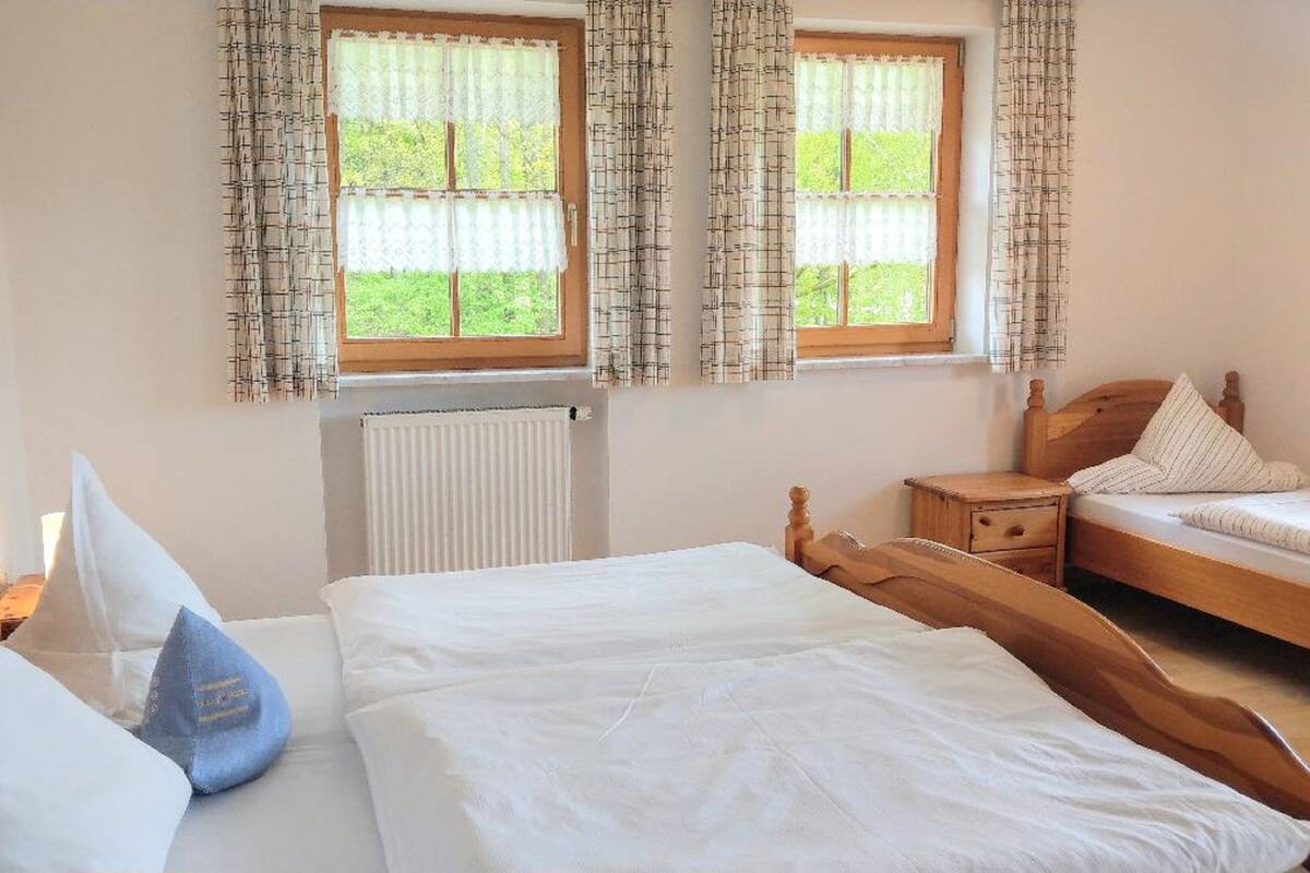 A bedroom with two beds, a wooden headboard, a bedside table, and a window with curtains.