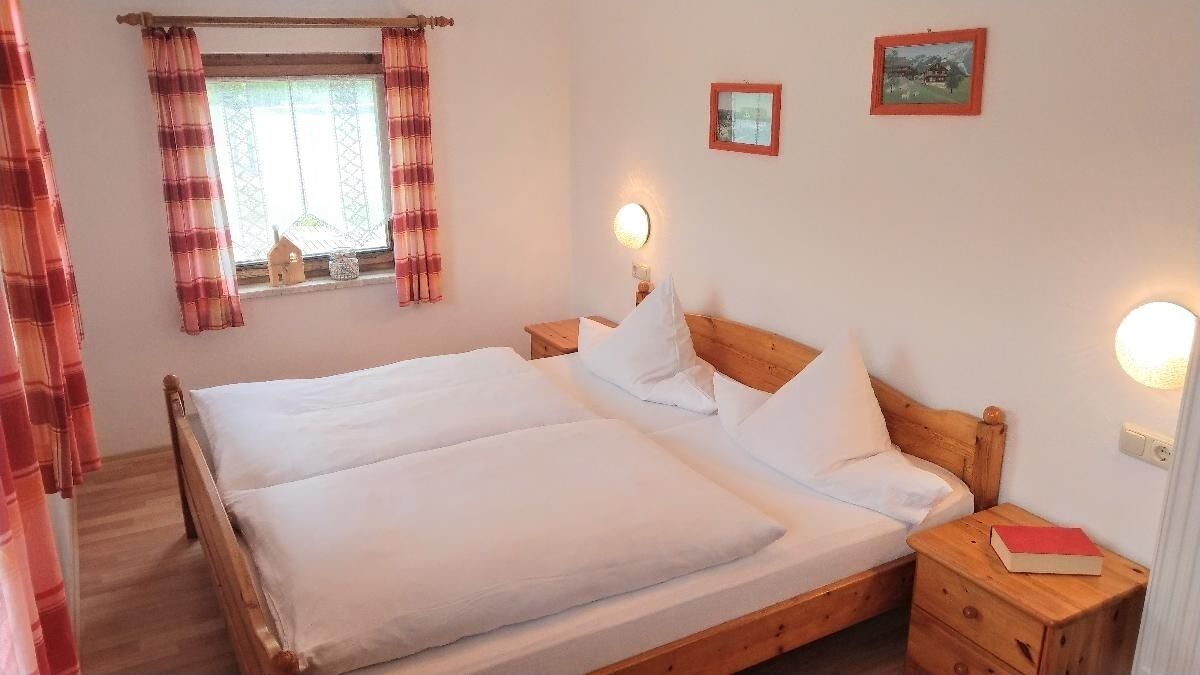 A double bed with white linens, two bedside tables with lamps, plaid curtains, and two small framed pictures on the wall.