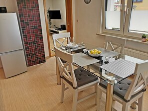 A compact kitchen with a refrigerator, a dining table with chairs, and a window with a view. - Ferienwohnung Andalucia (Selb)