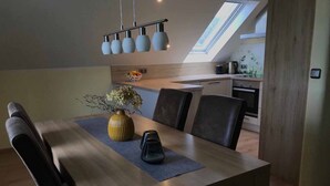 A dining area with a wooden table, chairs, a vase with flowers, and a skylight above. - Ferienwohnung Anna (Moosbach)