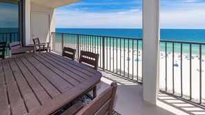 A balcony with a view of a beach, a table, and two chairs.