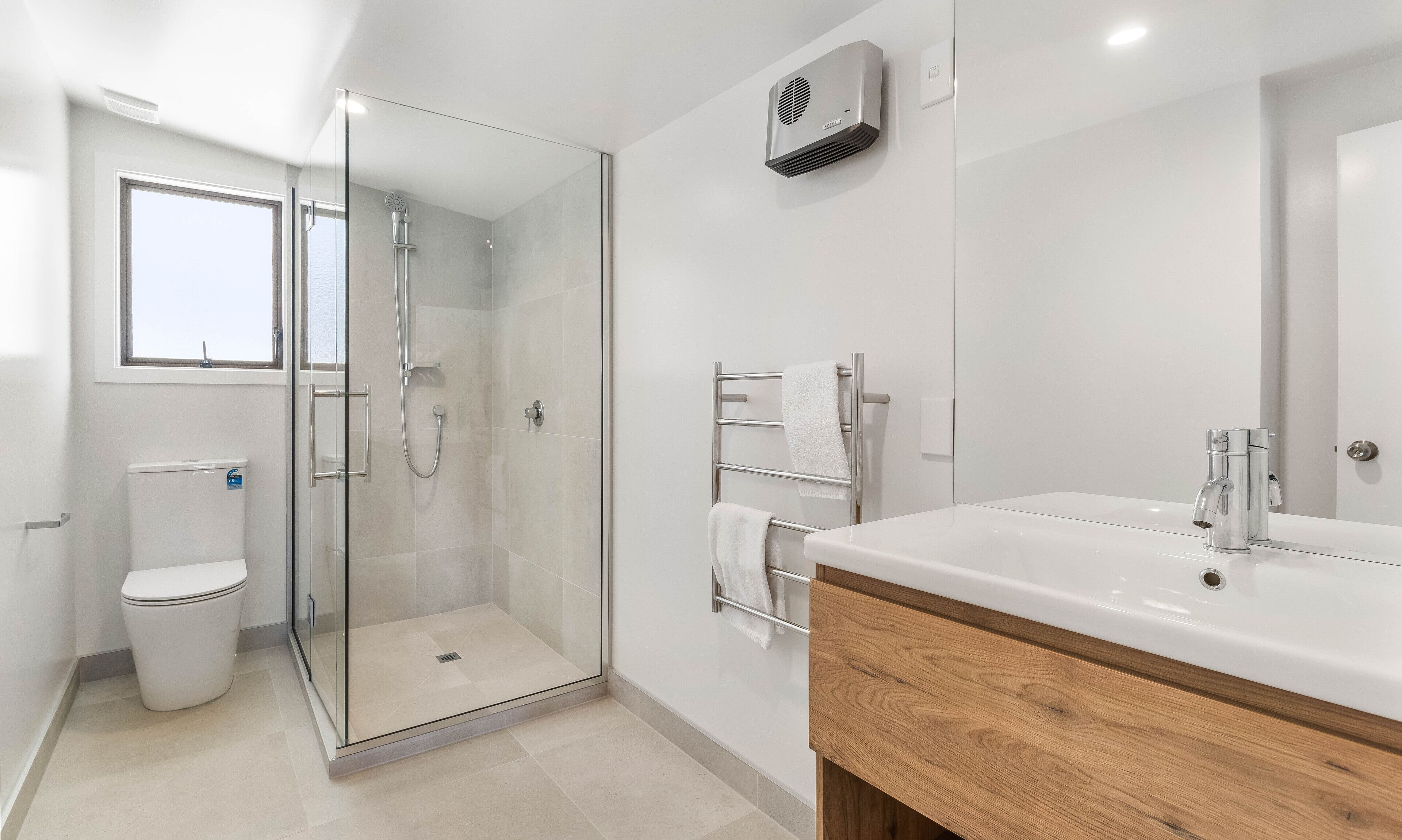 Un baño moderno con ducha envuelta en vidrio, inodoro blanco y tocador de madera con lavamanos.