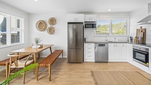 Une cuisine moderne avec des meubles blancs, des appareils en acier inoxydable et une table à manger en bois, accompagnée de bancs.