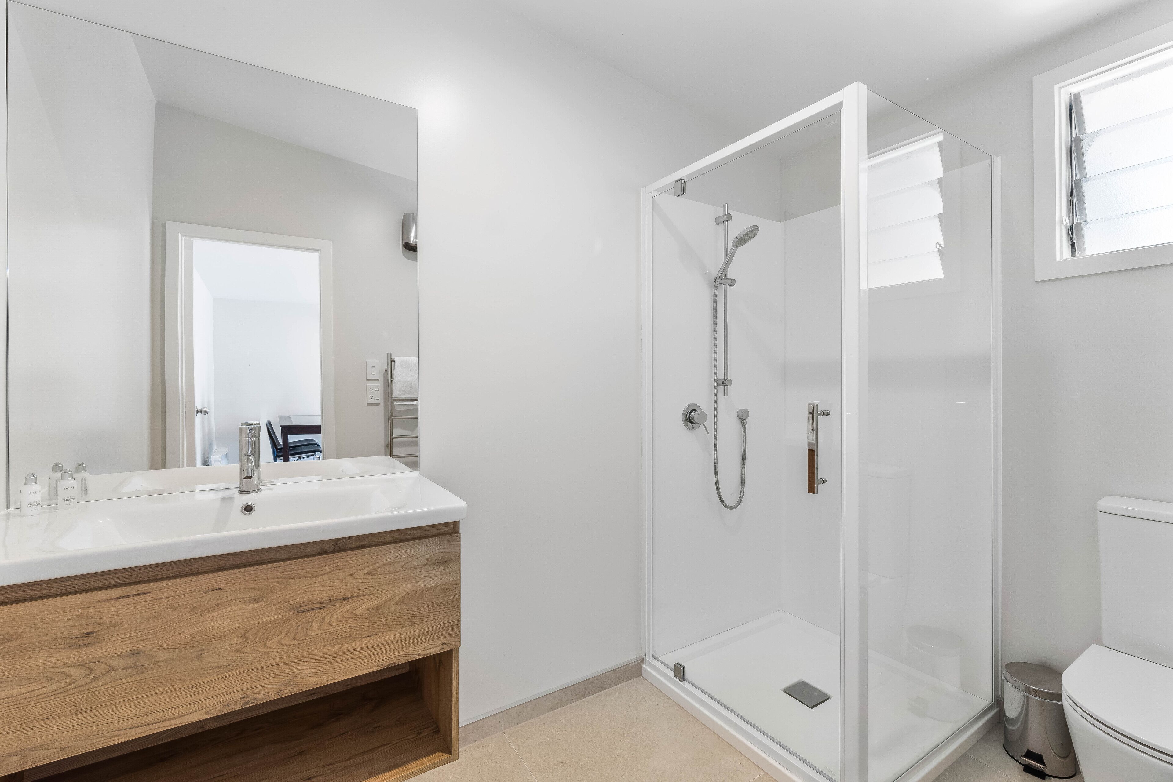 A modern bathroom with a wooden vanity, a glass shower enclosure, and a white toilet.