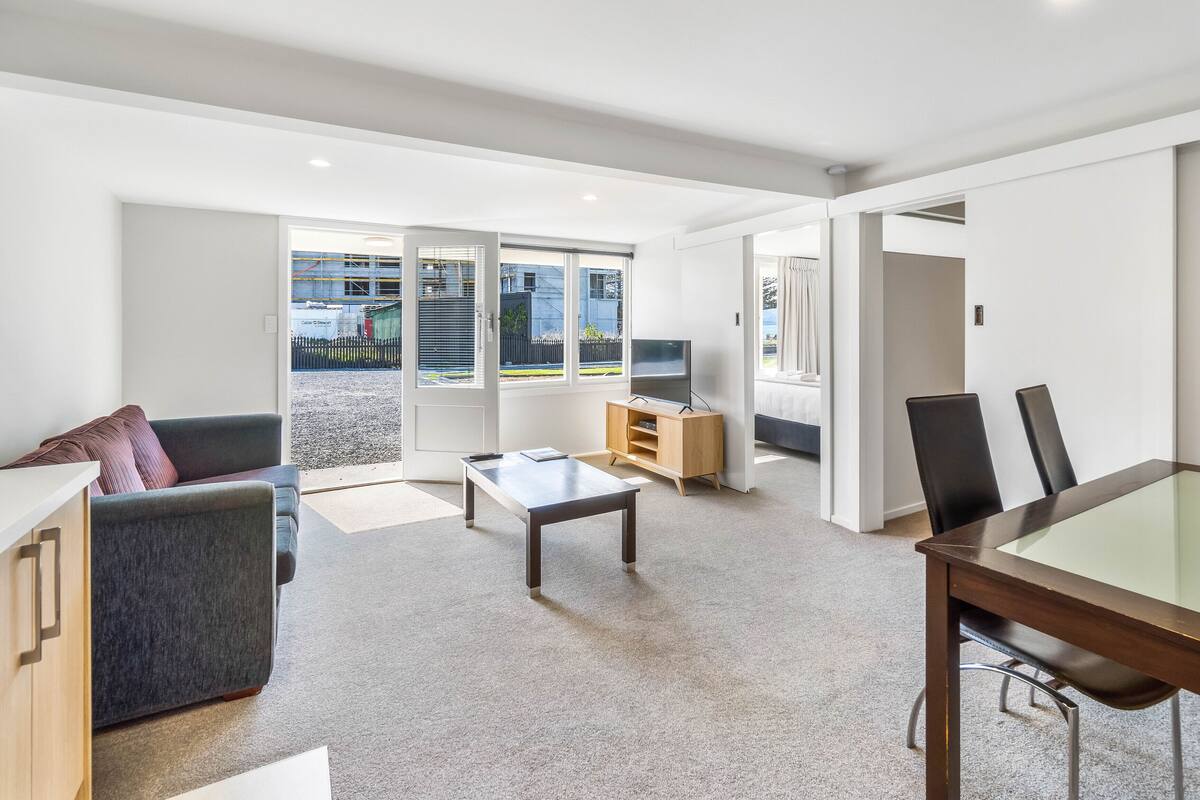 Un salon moderne comprenant un canapé, une table basse, un téléviseur posé sur un meuble en bois, et un coin repas avec une table et des chaises en verre.