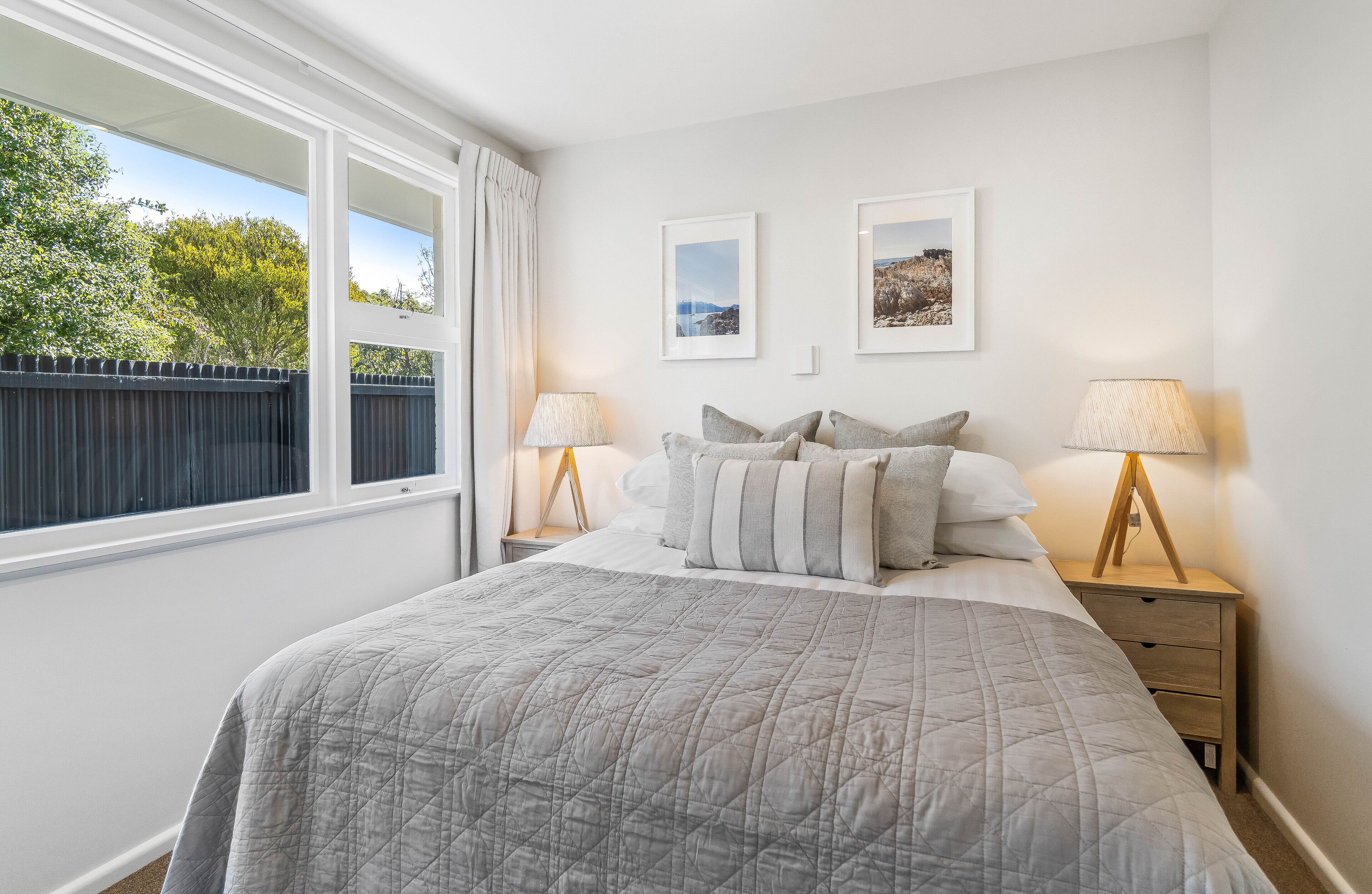 A bedroom with a large bed, two bedside tables with lamps, and framed pictures on the wall.