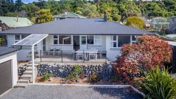 A house with a covered patio, stone steps, and a view of a forested hill.