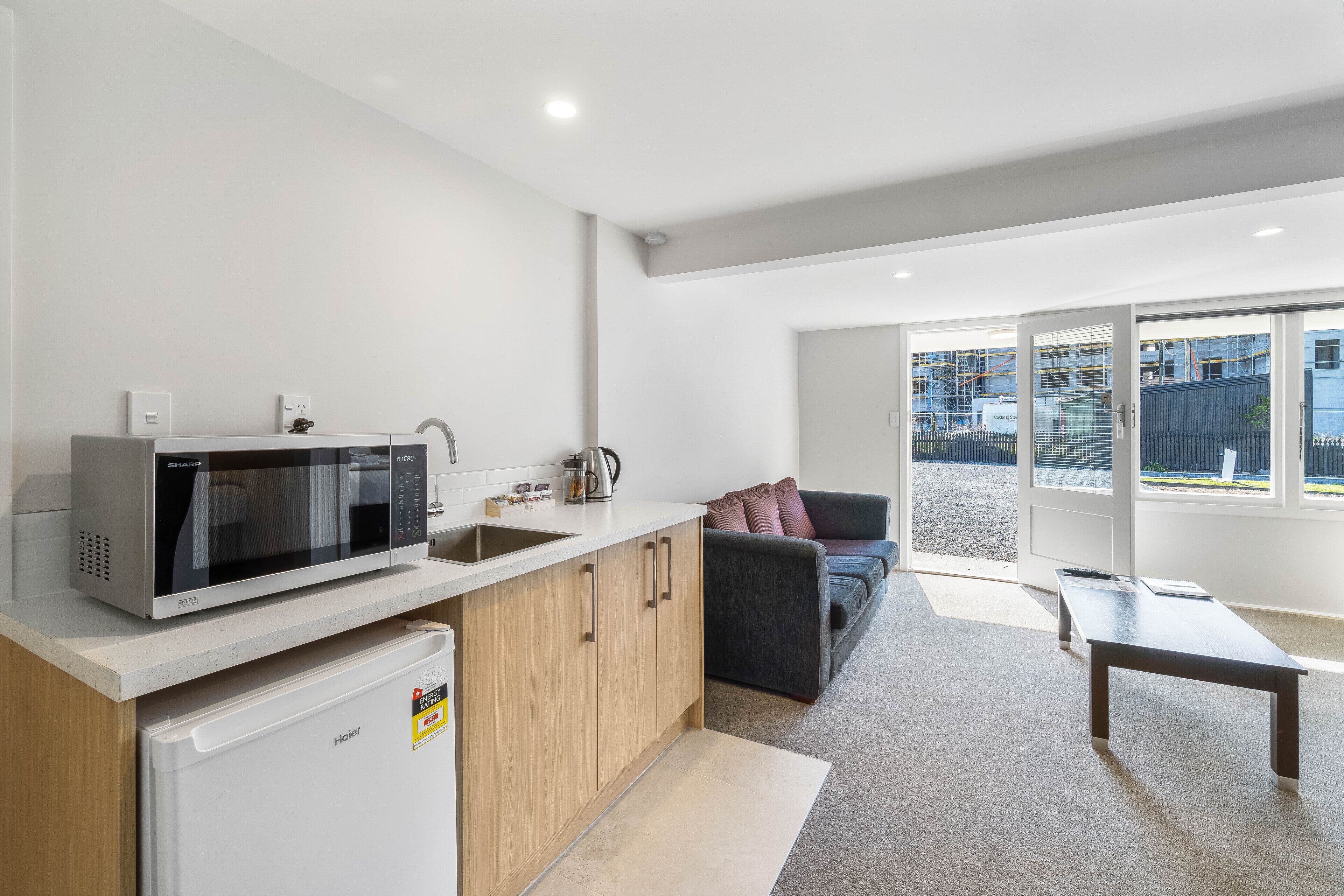 A compact kitchen with a microwave, coffee maker, and refrigerator. There is a dark-colored sofa and a small table in the living area.