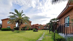 A row of wooden cabins with a stone pathway leading through a well-maintained lawn. - Haemaji Pension (Seogwipo)