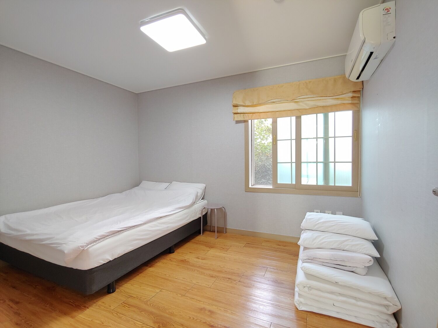 A small, clean room with a single bed, a window with a view, and a ceiling light.