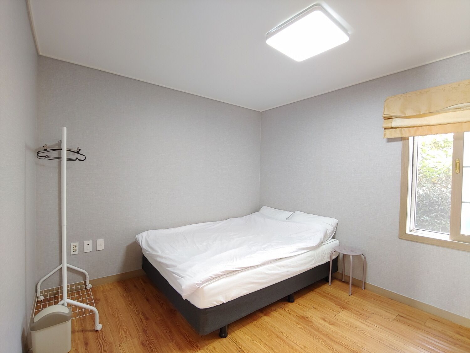 A bedroom with a bed, a window with curtains, a radiator, and a small table.
