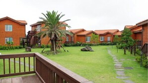 A row of wooden cottages with a grassy lawn and a wooden deck in the foreground. - Haemaji Pension (Seogwipo)