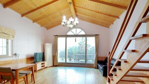 A spacious room with a wooden ceiling, a dining area with a table and chairs, a sofa, and a staircase. - Haemaji Pension (Seogwipo)