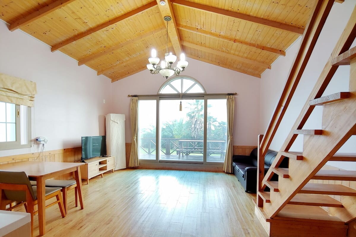Una habitación amplia con techo de madera, un comedor con mesa y sillas, un sofá y una escalera.