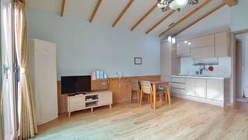 Een ruime woonkamer met houten vloer, een eettafel met stoelen, een televisie en een keuken met kastjes en een spoelbak.