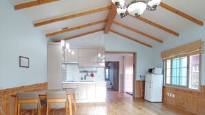 A spacious kitchen with wooden beams, a dining area with a table and chairs, and a view of the adjacent room. - Haemaji Pension (Seogwipo)