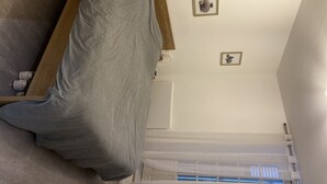 A bedroom with a bed, a wooden headboard, a window with blinds, and two framed pictures on the wall.