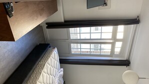 A bedroom with a bed, a window with curtains, a ceiling fan, and a remote control on a table.