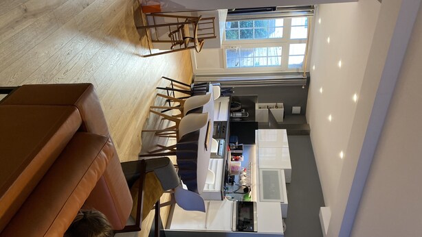 A modern kitchen with a dining area, wooden flooring, and a large window providing natural light.