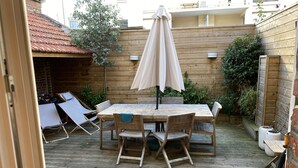 A wooden deck with a table and chairs, surrounded by a wooden fence and greenery.