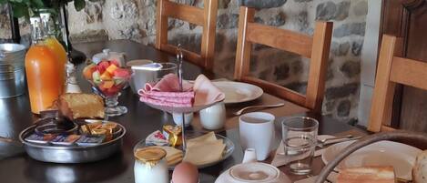 A breakfast table with various food items, a vase of flowers, and a stone wall in the background.