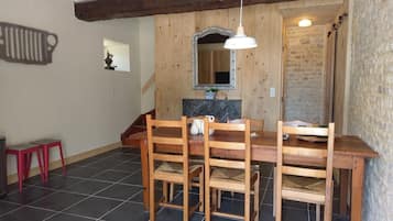 A dining area with a wooden table and chairs, a hanging light fixture, and a stone wall.