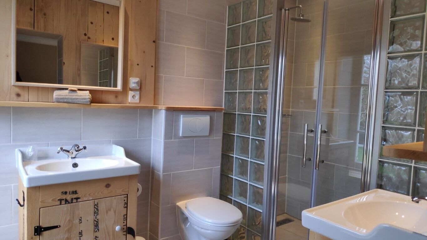 Une salle de bain avec un meuble en bois, un lavabo blanc, des toilettes et une cabine de douche en verre.