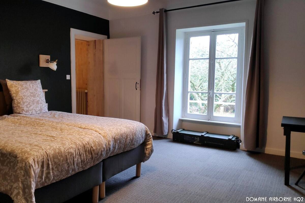 Een slaapkamer met een bed, een raam, een deur en een klein tafeltje.